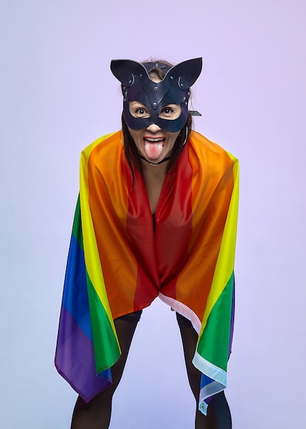 A woman in a cat mask holds a rainbow flag.