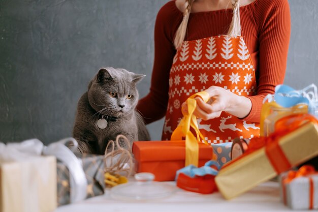 Woman and cat at the table are packing boxes with christmas gifts