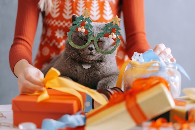 Woman and cat at the table are packing boxes with christmas gifts