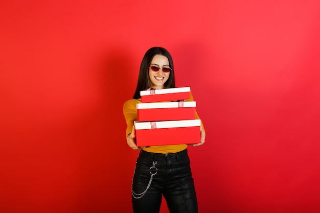 Woman celebrates birthday with many gifts isolated on red background.