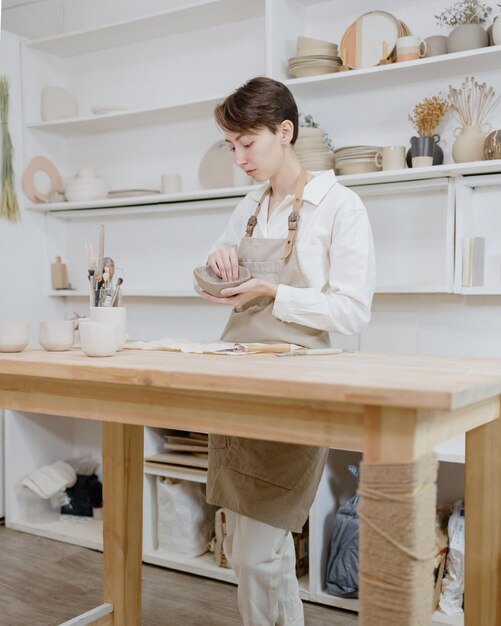 Woman ceramist in the workshop makes mugs out of clay small business or hobby is the creation of ceramic products