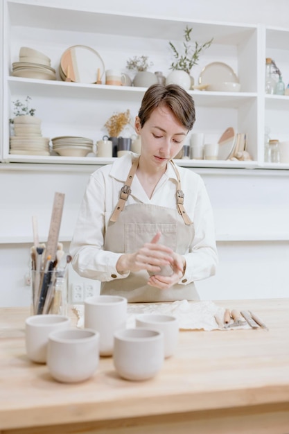 Woman ceramist in the workshop makes mugs out of clay small business or hobby is the creation of ceramic products