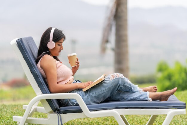 Woman on a chair listening to music while reading and drinking
a coffee