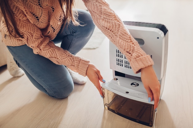 Woman changing water container of dehumidifier at home. 