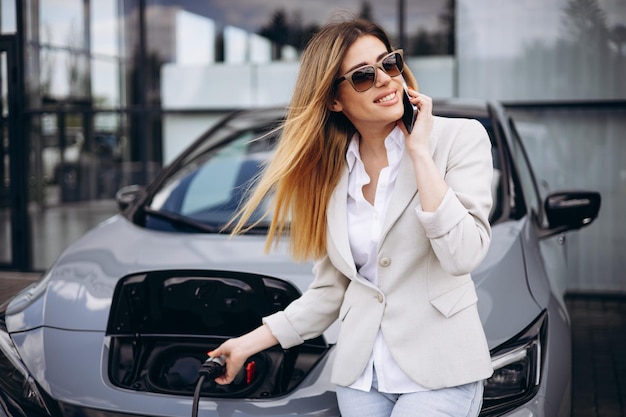 woman charging electric car at charging station and talking on the phone