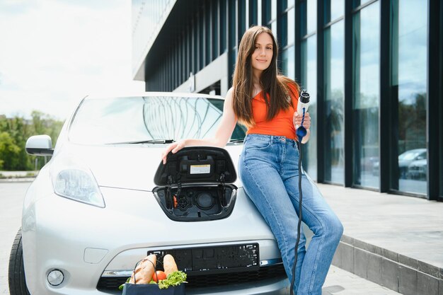 Женщина заряжает электро автомобиль на заправке