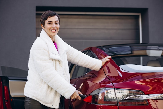 Woman charging electro car with charging pistol by the house