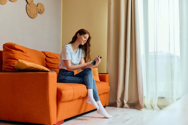 Woman chatting on the orange couch with a smartphone Lifestyle