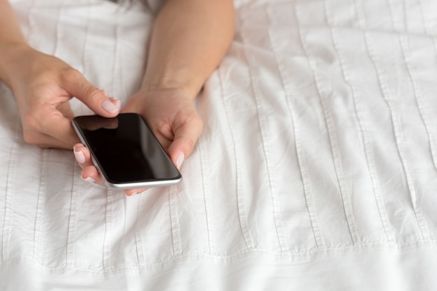 Woman checking the cell phone on the bed