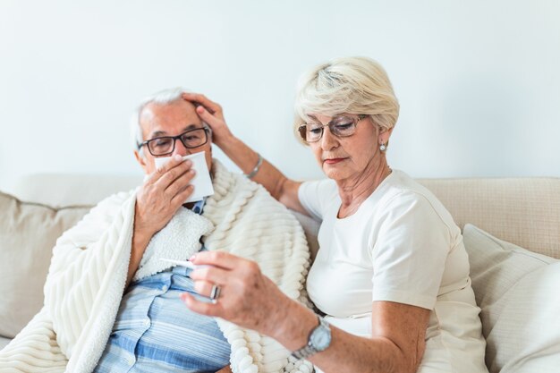 Woman checking fever temperature of senior man sitting on bed.