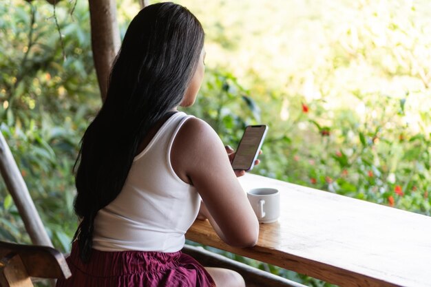 Photo woman checking her cell phone with a cup of coffee in the morning