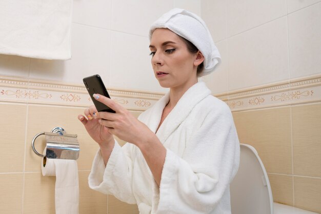 Photo woman checking her phone on the toilet