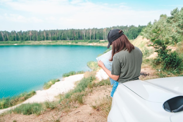 背景に青い水とsuv車のフード湖の地図でチェックする女性