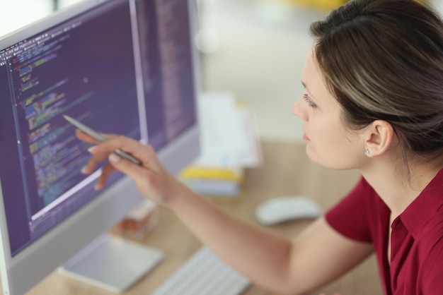 Женщина проверяет код, указывая ручкой на экран компьютера