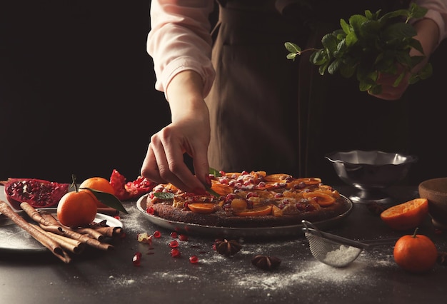 Woman chef decorating delicious tangerine pie on grey table