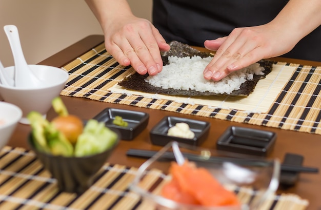 Cuoca donna che riempie gli involtini di sushi giapponesi con riso