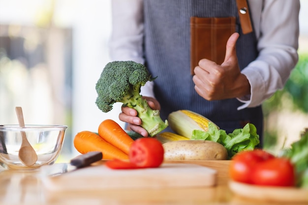 A woman chef holding and making thumb up to show good sign to a\
green broccoli with vegetables tray on the table