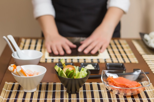 主要な食材を前景にした日本の巻き寿司を作る準備ができている女性シェフ