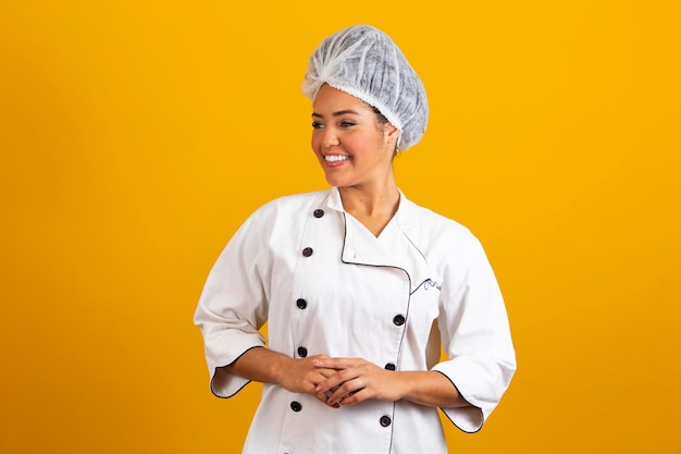 Chef donna che indossa l'uniforme e il cofano con le braccia in piedi incrociate e in posa su sfondo giallo isolato concetto di occupazione