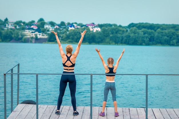 Woman and child are doing hands up exercises on the pier the lake