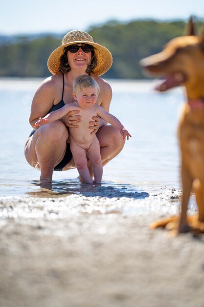 Женщина и ребенок играют в воде с собакой.
