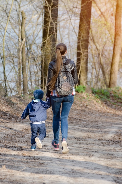 Woman and a child are walking along the road in the forest. View from the back