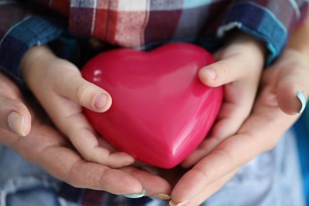 Woman and child hands holding red toy heart closeup