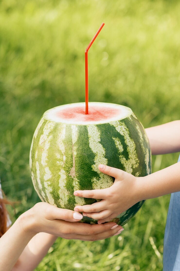 Woman and child hands holds a whole watermelon with cocktail straw close up.