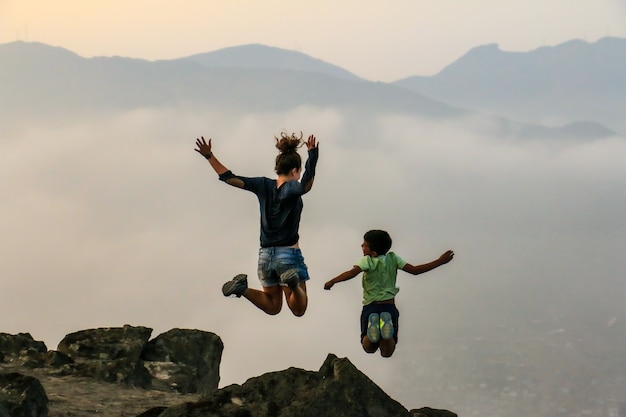 A woman and a child jump over a mountain cloudy background and other mountains