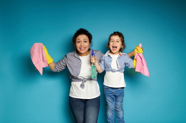 Woman and child posing on a blue surface with cleaning products in hands