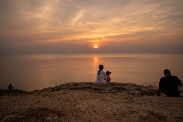 A woman and a child sit on a cliff, looking at the sunset.