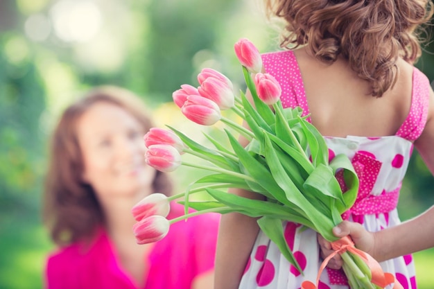 Woman and child with bouquet of flowers against green blurred background Spring family holiday concept Womens day