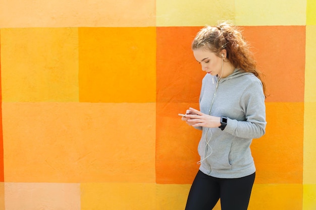 Woman choose music to listen in her mobile phone during jogging\
in city, copy space, colorful background