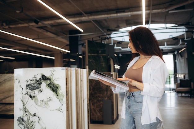 A woman chooses ceramic tiles in a hardware store A beautiful blonde in a black jacket touches samples in a showcase Repair and interior design