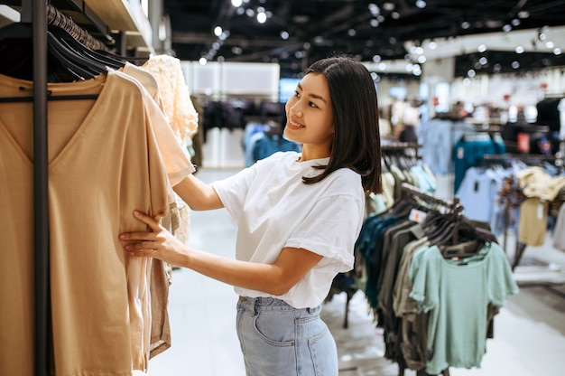 Женщина выбирает одежду в магазине одежды. Женщина, делающая покупки в модном бутике, шопоголик, покупатель, глядя на одежду
