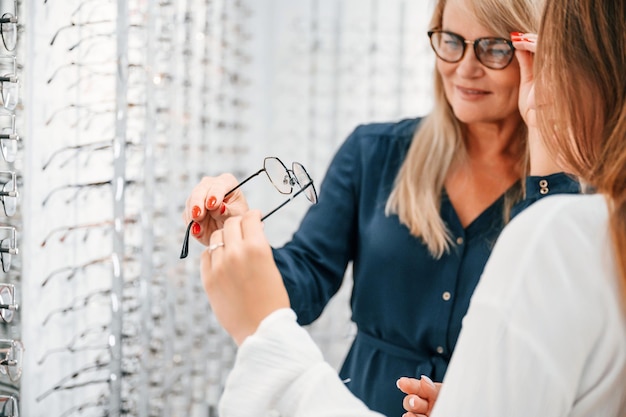 Woman choosing glasses in the store and getting help by assistant