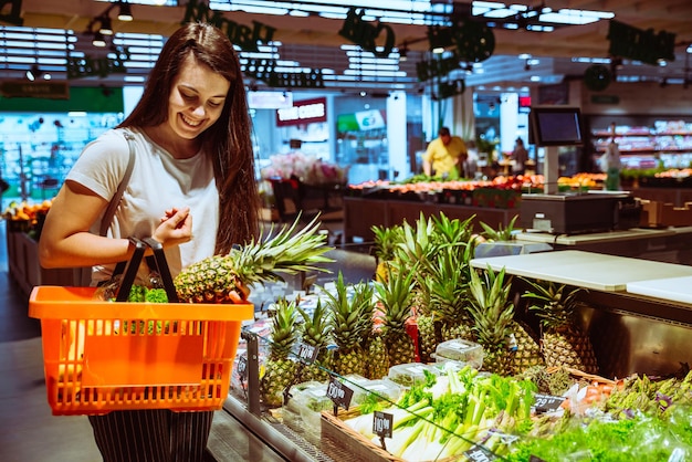 Женщина выбирает ананас в продуктовом магазине