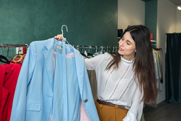 woman choosing stylish jacket or dress in clothing store