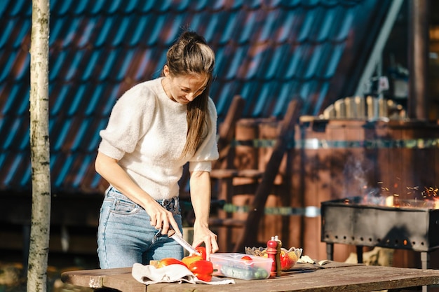 Woman chopping bell pepper for barbecue near tiny house