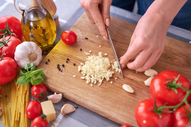 Woman chopping garlic on wooden cutting board at domestic kitchen