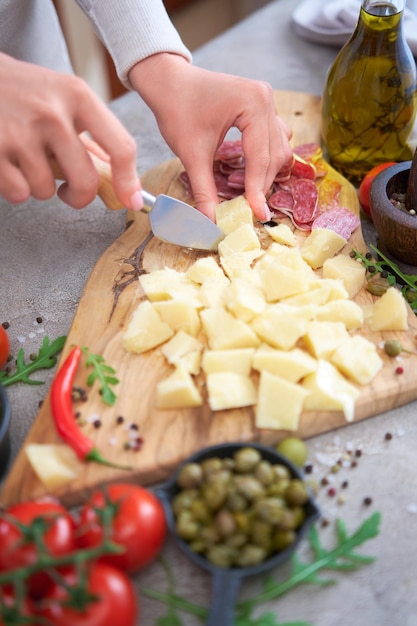 Woman chopping Parmesan cheese with knife on grey table at domestic kitchen