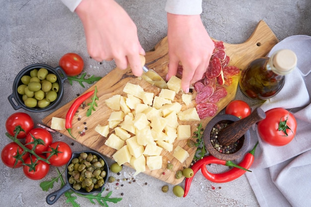 Woman chopping Parmesan cheese with knife on grey table at domestic kitchen