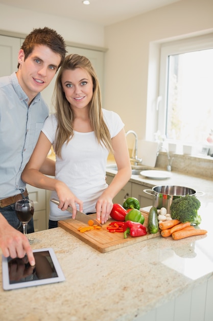 Woman chopping peppers with man typing on the tablet pc