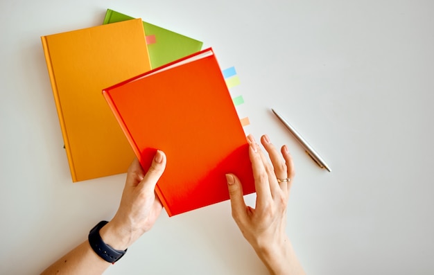 The woman chose a red notebook and was going to reveal it. Behind are orange and green notebooks. High quality photo
