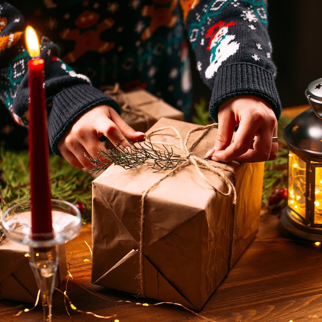 Женщина в рождественском свитере связывает подарочную коробку ремесла
