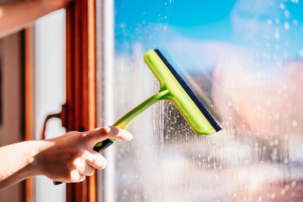 Woman clean a window with cleaning sprayer Housekeeping concept Girl hold in hand cleaning squeegee