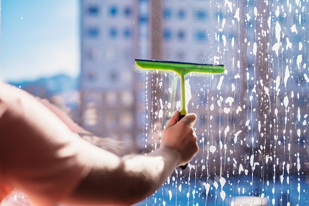 Woman clean a window with cleaning sprayer Housekeeping concept Girl hold in hand cleaning squeegee