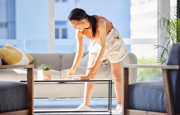 女性の掃除とラウンジでの整理の幸福と家事のためのホーム テーブルの本 フィリピンの家できちんとしたリビング ルームの本の配置に満足して清潔で幸せな女の子