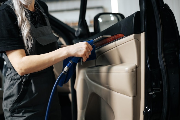 Donna che pulisce il salone dell'auto con spray lucidante nel servizio di dettagli dell'auto