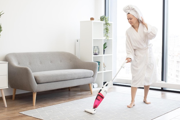 Woman cleaning carpet in living room with cordless vacuum